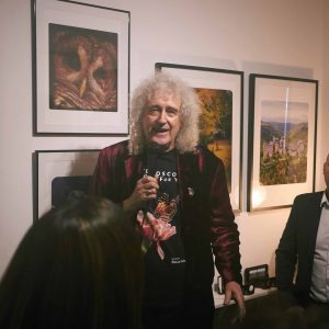 Photo of a man with curly grey hair speaking at a gallery opening featuring landscape and wildlife photography.