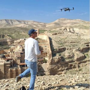 A man observing aerial drone footage of desert landscape with ancient city ruins and a drone flying overhead.